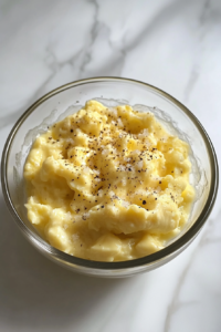 This image shows mashed egg yolks mixed into a creamy dressing with mayonnaise, vinegar, mustard, and seasoning in a glass bowl on a white marble countertop.