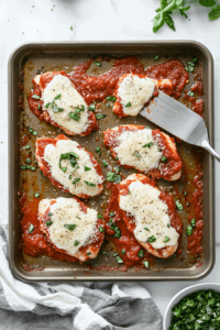 This image shows marinara sauce and shredded cheese being added to the chicken.