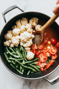 adding-cauliflower-green-beans-tomatoes-beef-broth-worcestershire-sauce-to-the-sauted-vegetables-in-the-crockpot