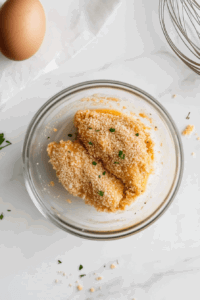 This image shows chicken pieces being coated with the parmesan mixture after dipping in egg.