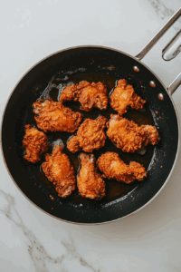 This image shows chicken pieces frying in a pan until golden brown.