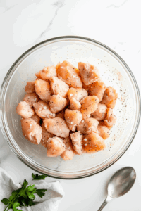 This image shows chicken thighs being mixed with oil and seasonings in a large bowl.