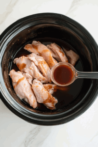 This image shows chicken placed in the crockpot with sauce poured over it
