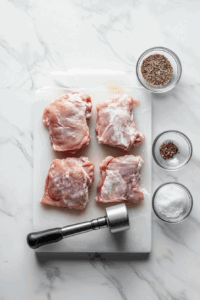 This image shows four chicken breasts being pounded to a ¼-inch thickness and seasoned with salt, pepper, and garlic powder.
