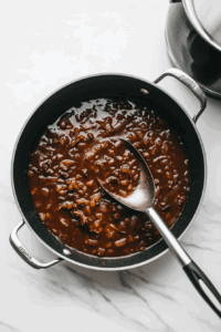 This image shows a pan being deglazed with liquid, scraping up browned bits to create a rich base for the soup.