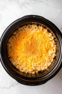 sprinkling-the-remaining-cheese-over-the-top as the last layer for gooey and melty touch in crockpot macaroni and cheese