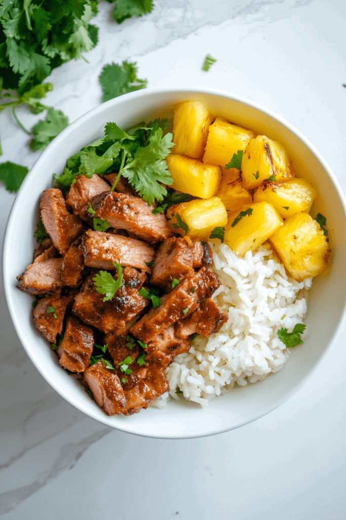 Tender bite-sized pieces of pork served in a white bowl alongside fluffy rice, garnished with fresh cilantro, capturing the essence of Al Pastor flavors.