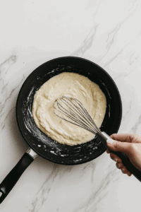This image shows heavy whipping cream being added to the skillet