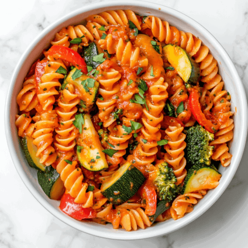 this image shows A delicious plate of 20-minute pasta with vegetables, featuring a rich red creamy sauce and vibrant broccoli florets, yellow and red bell peppers, and round-shaped zucchini pieces, making for a colorful and flavorful meal.