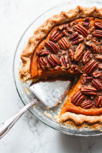 This image shows a knife slicing through the sweet potato pecan pie, revealing its creamy filling and crunchy topping.