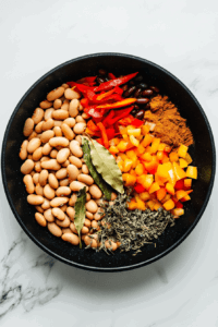 This image shows beans being added to a pot along with a medley of vibrant spices, enhancing the soup with rich flavors and hearty textures.