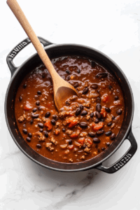 This image shows black beans with their liquid, tomatoes, salsa, cumin, and chili powder being combined in a large pot, forming the base of a flavorful black bean soup.