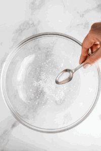 This image shows cream of tartar being added to the drained chickpea liquid to help stabilize the whipped cream during the whipping process.