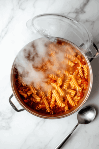this image shows Fresh basil leaves being added on top of the creamy tomato pasta in the pot, with a final adjustment of salt and pepper for a flavorful finish.