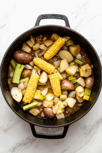 This image shows fresh corn kernels and juices from the cobs being stirred into a mixture of vegetables in a Dutch oven, intensifying the sweet and savory flavors of the chowder.