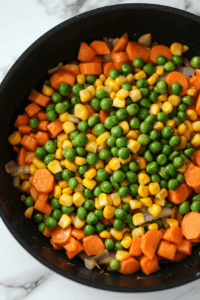 this image shows A vibrant mix of peas and corn being added to the creamy sauce in the pot, enhancing the vegan chickpea pot pie pasta with a pop of color and sweetness.