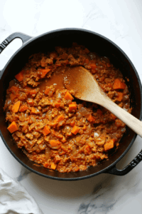 This image shows diced sweet potatoes and a blend of spices being added to a soup pot, building the rich and flavorful base for the vegan sweet potato soup.
