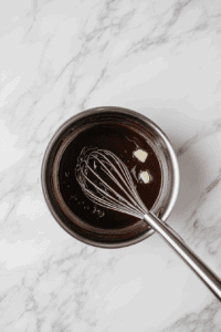 This image shows vegan butter being added to the coconut milk and sugar mixture, enriching the texture of the filling for the Vegan Sugar Cream Pie.