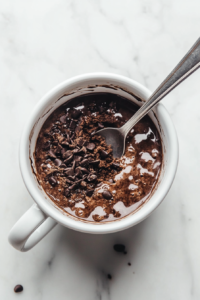 This image shows wet ingredients like milk, oil, and vanilla being poured into the mug containing dry ingredients, ready to be mixed into a smooth batter.