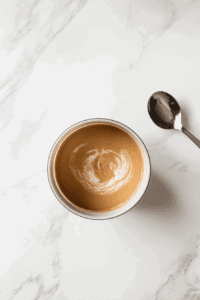 this image shows Water being added to the peanut sauce while whisking to achieve the perfect creamy consistency for drizzling over the noodles.