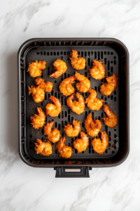 This image shows shrimp arranged in an air fryer basket, cooking at 360°F to achieve a perfectly crisp coating.