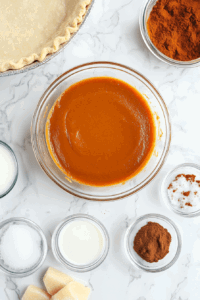 This image shows various ingredients, including pumpkin purée, brown sugar, and spices, neatly arranged on a countertop, ready to be combined for the vegan pumpkin pie filling.