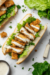 The final step of layering crispy chickpea patties, fresh lettuce, and vegan Caesar dressing on a toasted bun to create a perfect sandwich.