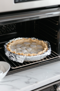 This image shows the pie crust being baked in the oven until it turns golden brown, providing a crisp and flaky base for the coconut cream filling.