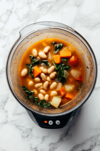 This image shows half of the soup being blended in a mixer, creating a smooth texture while preserving the hearty chunks of vegetables and beans.