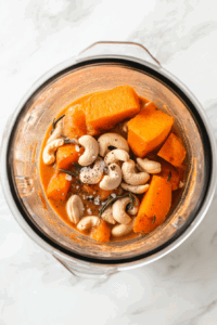 this image shows A blender filled with roasted sweet potatoes, shallots, garlic, soaked cashews, balsamic vinegar, tomato paste, and seasonings being blended into a smooth, creamy sauce.