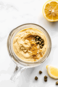 A blender filled with ingredients like cashews, lemon juice, and garlic being blended into creamy vegan Caesar dressing.