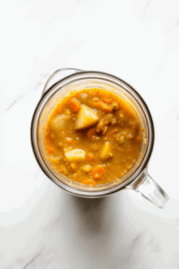 This image shows a blender filled with the cooked soup ingredients, being blended into a smooth and creamy consistency for the vegan broccoli cheese soup.