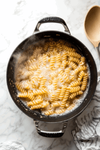 this image shows A pot of boiling water with pasta being added, the first step in preparing the vegan chickpea pot pie pasta.