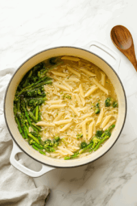 this image shows A pot of boiling water containing penne pasta, sliced carrots, and broccoli florets, the first step in preparing a vibrant Vegan Pasta Primavera.