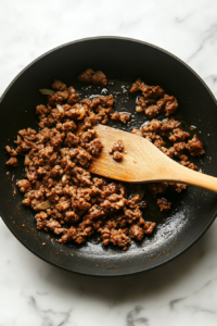 This image shows sausage being cooked in a skillet, browned evenly to create a flavorful base for the Crockpot Lasagna.
