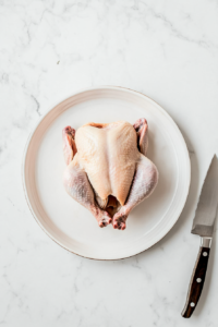 this image shows A raw whole chicken is shown being prepared by patting it dry with paper towels, an essential step before applying spices and cooking.
