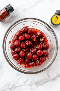 This image shows a bowl of cherries being mixed with juice, ensuring the cherries soak thoroughly to absorb the rich and tangy flavors, perfect for a flavorful dish.