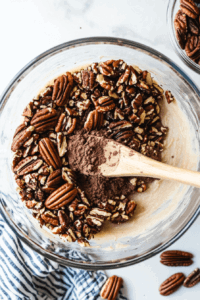 this image shows ground pecans, blended date paste, and a drizzle of coconut oil being mixed in a bowl to form a cohesive, rich crust mixture for the chocolate truffle pie.