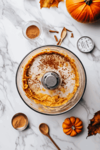 This image shows organic pumpkin purée, arrowroot powder, maple syrup, and warm spices being blended together in a bowl to create a rich, velvety filling for the pumpkin pie.