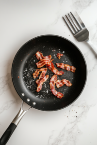 This image shows crispy strips of bacon being cooked in a frying pan until golden brown, forming the savory base for the salad.