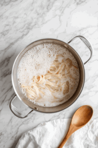 this image shows Brown fettuccine boiling in a pot of water, being stirred with a spoon to cook evenly for the sweet potato pasta dish.