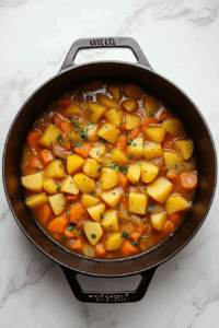 This image shows diced carrots and Yukon Gold potatoes cooking with seasonings in a pot, blending together for a hearty and flavorful vegan broccoli cheese soup base.