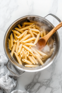 this image shows A large pot of boiling water with pasta being cooked to al dente, forming the base for the Roasted Red Pepper Cashew Cream Pasta.