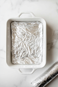 This image shows the baking dish covered tightly with aluminum foil, preparing the rolls for baking.