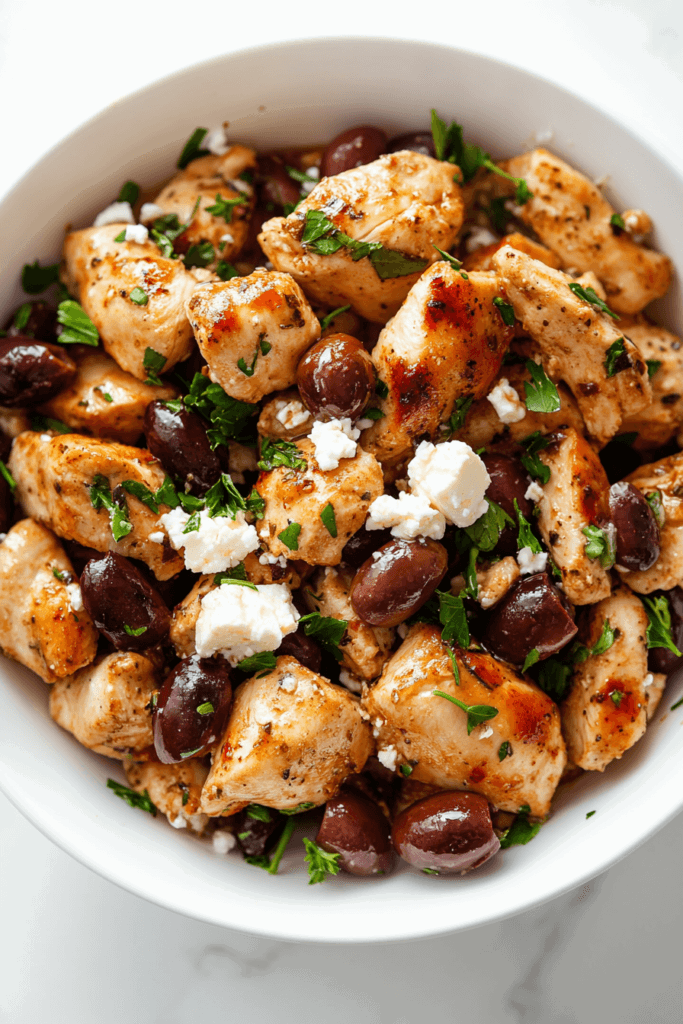 this image shows savory dish of crockpot Greek chicken, enriched with tender red beans and topped with melted shredded cheese, served in a white bowl.