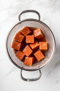 This image shows boiled sweet potatoes being poured into a colander in the sink, allowing the water to drain completely.
