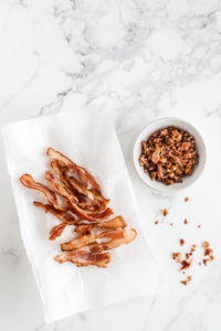 This image shows cooked bacon being drained on a paper towel and crumbled into small, bite-sized pieces for adding to the salad layers.