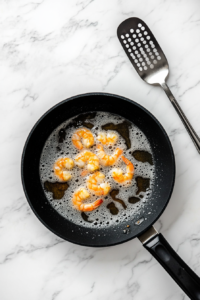 This image shows shrimp sizzling in hot peanut oil, achieving a perfectly golden and crispy texture for the Po'Boy sandwich.