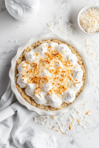 This image shows toasted coconut shavings being sprinkled generously over the creamy coconut pie filling, adding a decorative and flavorful finishing touch.