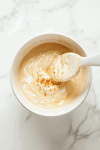 This image shows a serving of curried cauliflower sweet potato soup in a bowl, beautifully garnished with a swirl of coconut milk and a light dusting of powdered cinnamon for a sophisticated touch.